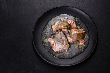 Canned sardine in oil on a black round plate against a dark concrete background