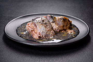 Canned sardine in oil on a black round plate against a dark concrete background