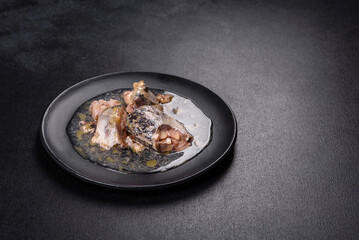 Canned sardine in oil on a black round plate against a dark concrete background