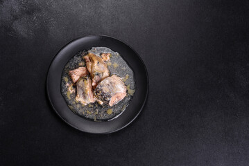 Canned sardine in oil on a black round plate against a dark concrete background