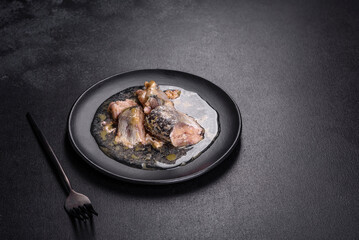 Canned sardine in oil on a black round plate against a dark concrete background