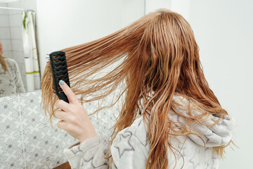 Naklejka premium A woman combs her wet tangled hair after a bath. View from the back