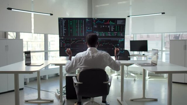 Back view of trader look at computer monitors and do winner gesture