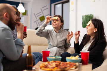 Businesspeople playing charades game and having fun together at office party, using sticky notes on forehead for guessing activity. Man and women enjoying drinks after work hours.