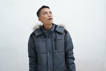 Asian man wearing winter jacket over isolated white background. looking up while gawking