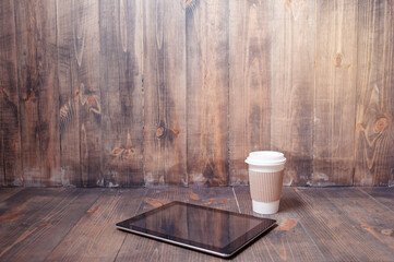 Every day essentials. Paper cup of coffee and tablet computer on the wooden background.