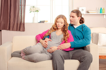 Fototapeta premium Young caucasian couple expecting a baby lying on the couch while enjoying the moment