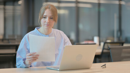 Young Woman with Laptop Reading Documents in Office 