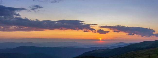 Beautiful sunset in the mountains. Evening twilight in the summer Carpathians. Elongated clouds over blue hills