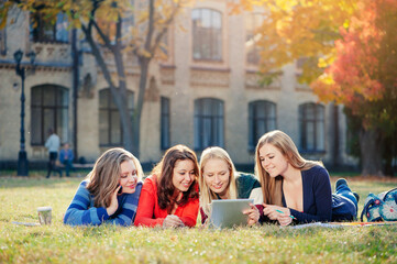 Surfing the net together. Four happy caucasian young woman looking at tablet pc and smiling while  they rest on grass at campus together