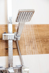 close-up of a chrome-plated shower, hanging on the wall, water pouring out of it