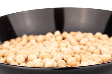 Several uncooked hummus grains in a black ceramic plate, close-up, isolated on white.