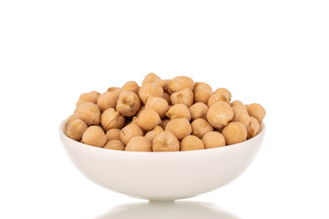 Several uncooked hummus grains in a white ceramic saucer, close-up, isolated on white.