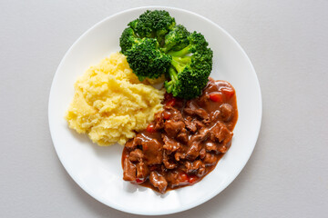 Beef stew on a plate with boiled potatoes and green broccoli