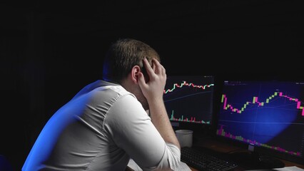 Side view of a man sitting at a computer and looking at an online stock market chart showing bitcoin currencies. The man is desperate from the fall of Bitcoin. In real time. Cryptocurrency. Investors