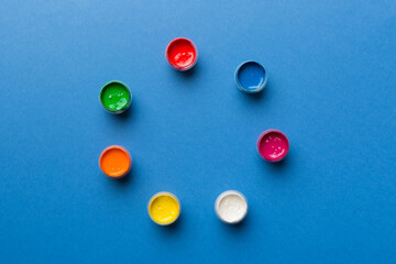 jars with gouache of different colors on Colored background. hobby painting. Top view with empty space. workplace for creativity. home teaching concept drawing