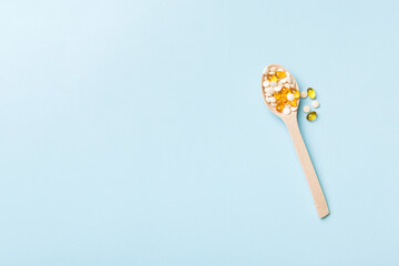 Vitamin capsules in a wooden spoon on a colored background. Pills served as a healthy meal. Drugs, pharmacy, medicine or medical healthycare concept