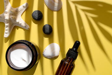 Clean brown glass cosmetic bottles with pipette jar of cream starfish sun shade from tropical leaf on yellow background. Summer concept of natural cosmetics. Spa products for health, beauty. Serum