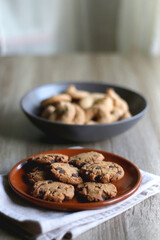 Plate of chocolate chip cookies and bowl of sugar cookies on wooden table. Selective focus.