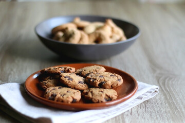 Plate of chocolate chip cookies and bowl of sugar cookies on wooden table. Selective focus.