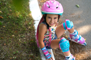 The girl was riding roller canyons and sat down to rest. A happy cute child in a protective helmet...