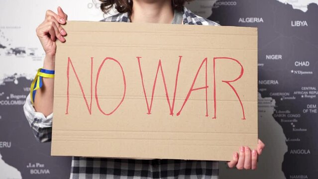 Young Ukrainian woman protesting against military conflict raises pacifist banner with inscription massage text "No war" on background of world map. Crisis, peace, stop aggression, woman against war
