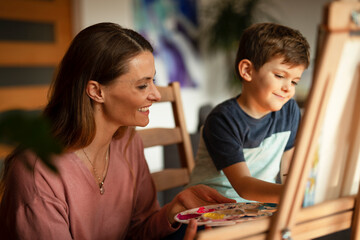 Mother and son painting at home. Little boy drawing with mom in living room