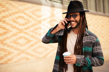 Handsome guy drinking coffee while walking in the street. Modern fashion man using the phone