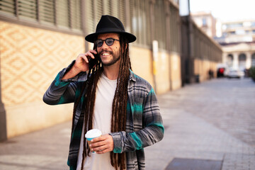 Handsome guy drinking coffee while walking in the street. Modern fashion man using the phone