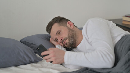 Obraz premium Man using Smartphone while Sleeping in Bed
