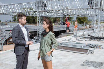 Event managers discuss stage construction. Installation of stage equipment and preparing for a live concert open air. Event manager portrait. Summer music city festival. Teamwork.