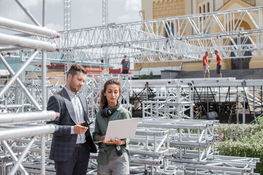 Event managers discuss stage construction. Installation of stage equipment and preparing for a live concert open air. Event manager portrait. Summer music city festival. Teamwork.