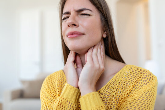 Close up of young woman rubbing her inflamed tonsils, tonsilitis problem, cropped. Woman with thyroid gland problem, touching her neck, girl has a sore throat