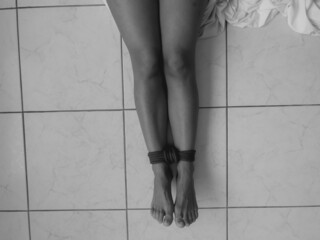 The girl is sitting on the floor with her legs tied with a rope. Sexual bondage. Soft focus