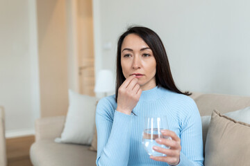 Asian woman takes pill with glass of water in hand. Stressed female drinking sedated antidepressant meds. Woman feels depressed, taking drugs. Medicines at work
