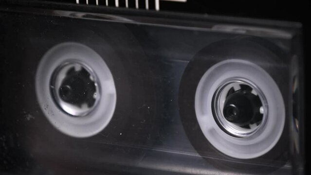 Audio cassette playing and rotates in deck of old tape recorder. Transparent audiocassette in retro player spinning. Close-up. Retro call recording, playback, reel playing, vintage technology 80s, 90s