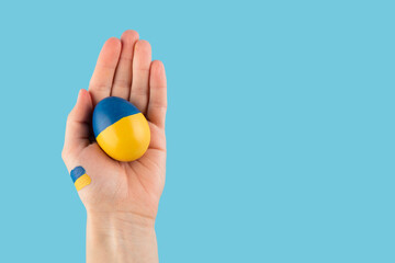 Easter egg in woman hand on Ukraine flag colors as concept for war Ukraine