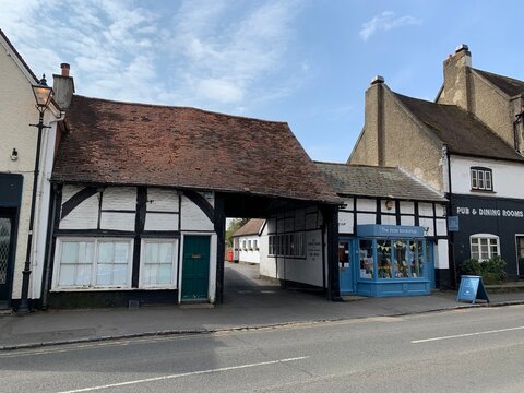 COOKHAM, ENGLAND - 30.04.2021. Street view of old town. Small cozy bookshop with blue door and shop window is allocated in medieval half timbered house on a High Road. Old pub to the right. Blue sky.