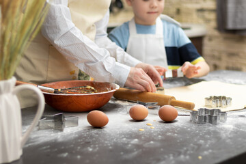 Mom and son are cutting out molds for baking sweet cookies from puff pastry on a black wooden table sprinkled with flour at home in the kitchen. Selective focus. Close-up