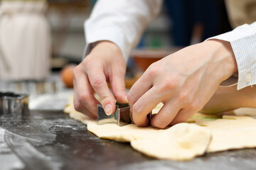 The female hands of the cook cut out the forms for baking sweet cookies from puff pastry on a black wooden kitchen table sprinkled with flour. Selective focus. Close-up