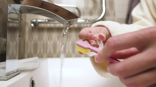 Close-up of unrecognizable caucasian young woman toothbrushing her kappa aligner under running water in bathroom sink. Care of dental accessories