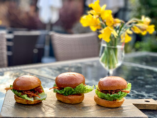 Lunch time three mini burgers on a wooden chopping board on the table with yellow flowers in a...