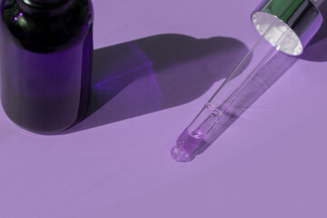 close up of pipette with pouring liquid serum and shadows on purple background
