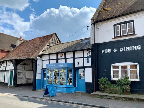 COOKHAM, ENGLAND - 30.04.2021. Street view of old town. Small cozy bookshop with blue door and shop window is allocated in medieval half timbered house on a High Road. Old pub to the right. Blue sky.