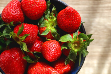 Bowl of fresh strawberries on wooden table, illuminated by sunlight. Flat lay.