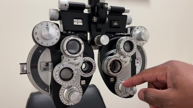 African American Man adjusting dials on phoropter used for eye examination or testing for eye glasses in ophthalmology, optometry, and optician offices
