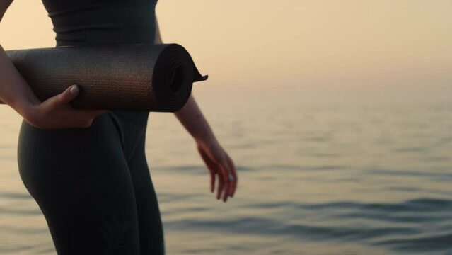 Closeup fit woman walking seashore with sport mat. Sporty woman going workout.