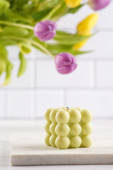 Pale green bubble candle on marble board with spring flowers - yellow and purple tulips