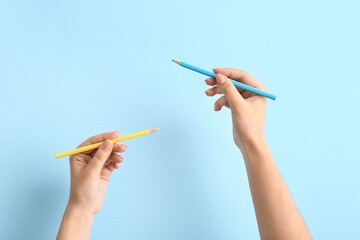 Female hands with pencils in colors of Ukrainian flag on blue background