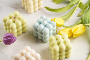 Many bubble candles - off-white, beige-colored and blue - on marble board with spring flowers - yellow and purple tulips